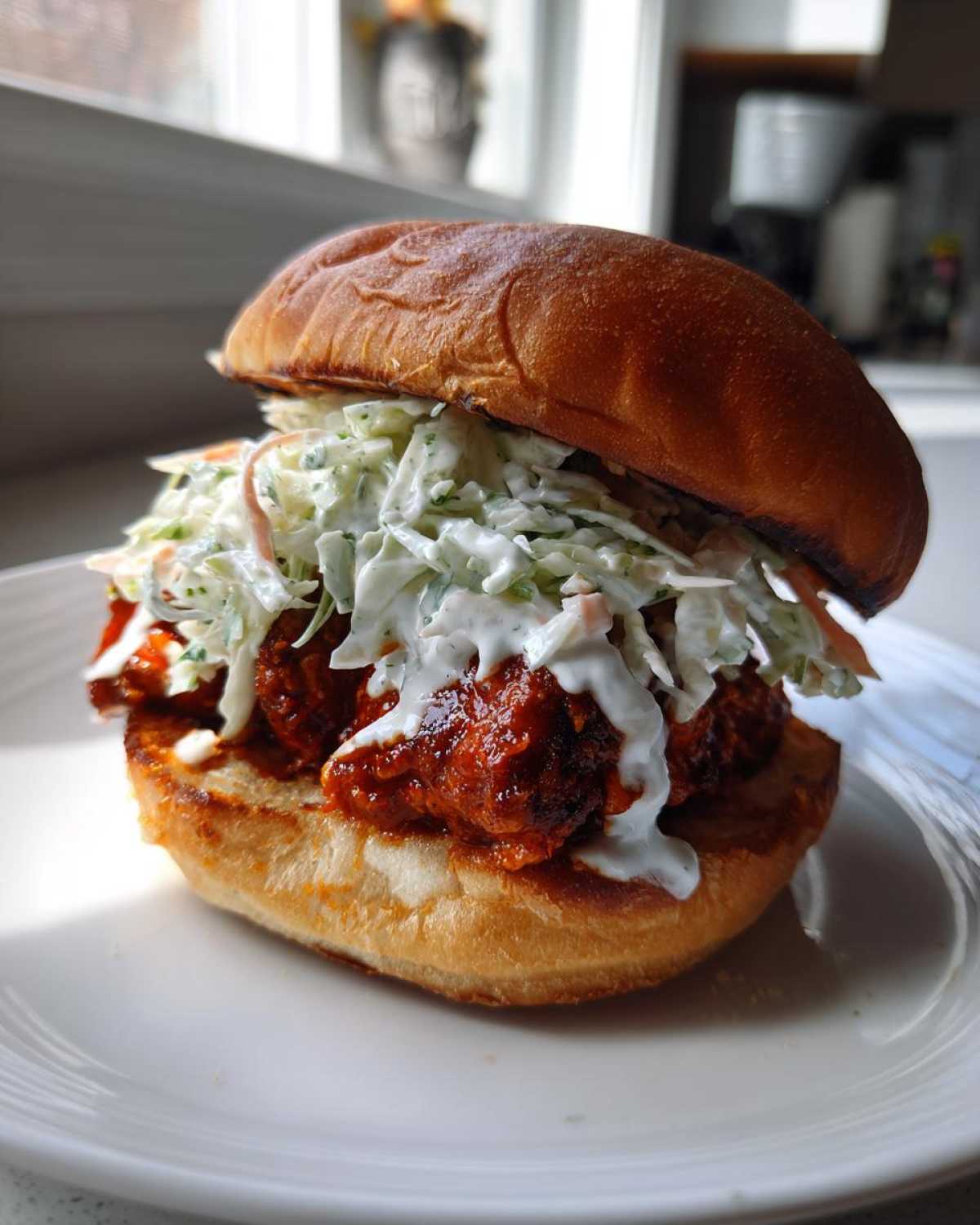 Close-up of a juicy buffalo chicken sandwich piled high with creamy coleslaw on a toasted bun.