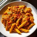 Close-up of creamy, orange-sauced cajun chicken pasta with penne, chicken pieces, and parsley garnish.