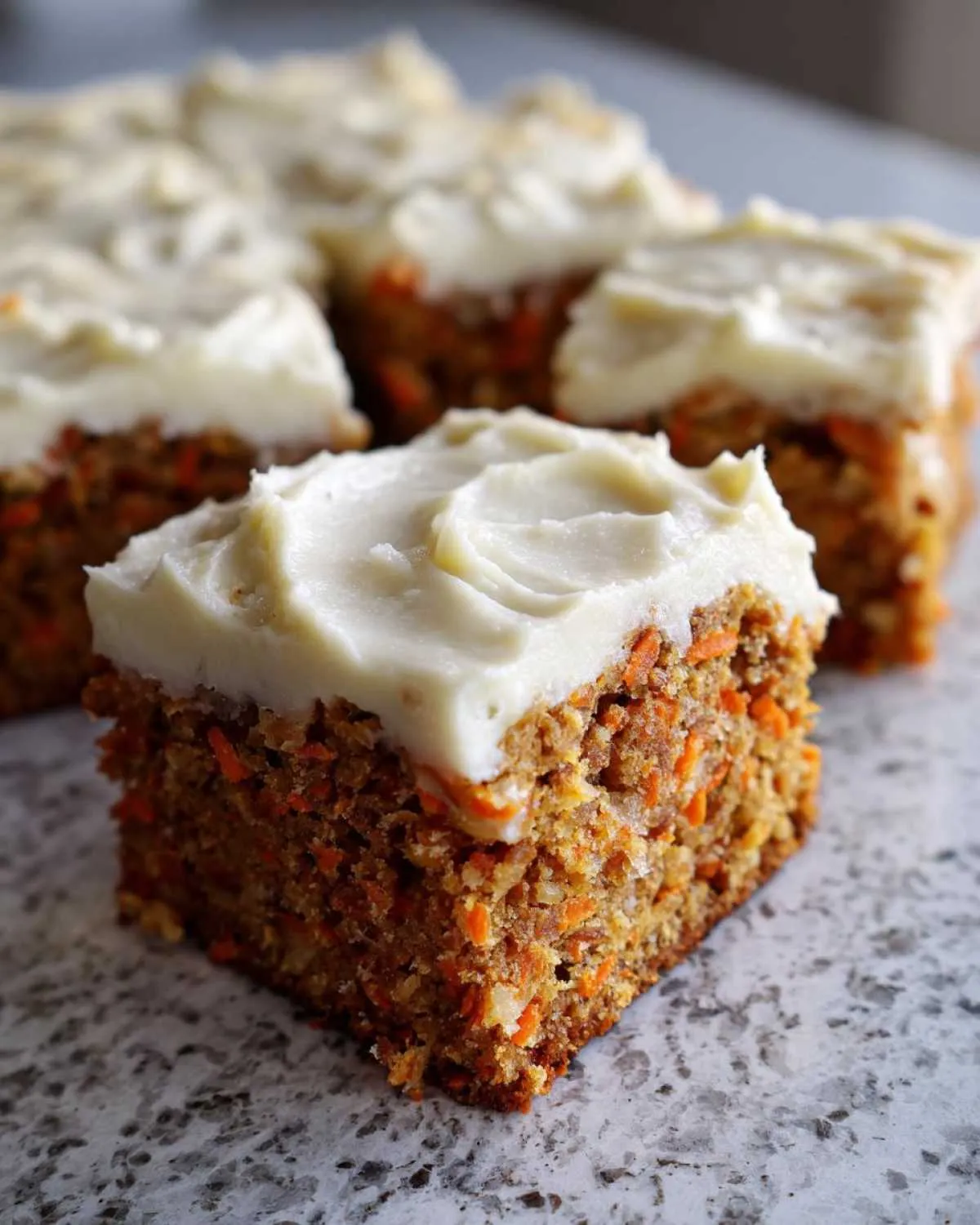 A square serving of moist carrot cake bars topped with thick cream cheese frosting.