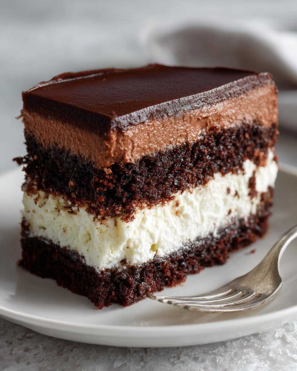 A rich slice of chocolate Italian love cake featuring dark cake layers, white cream filling, and chocolate mousse topping.