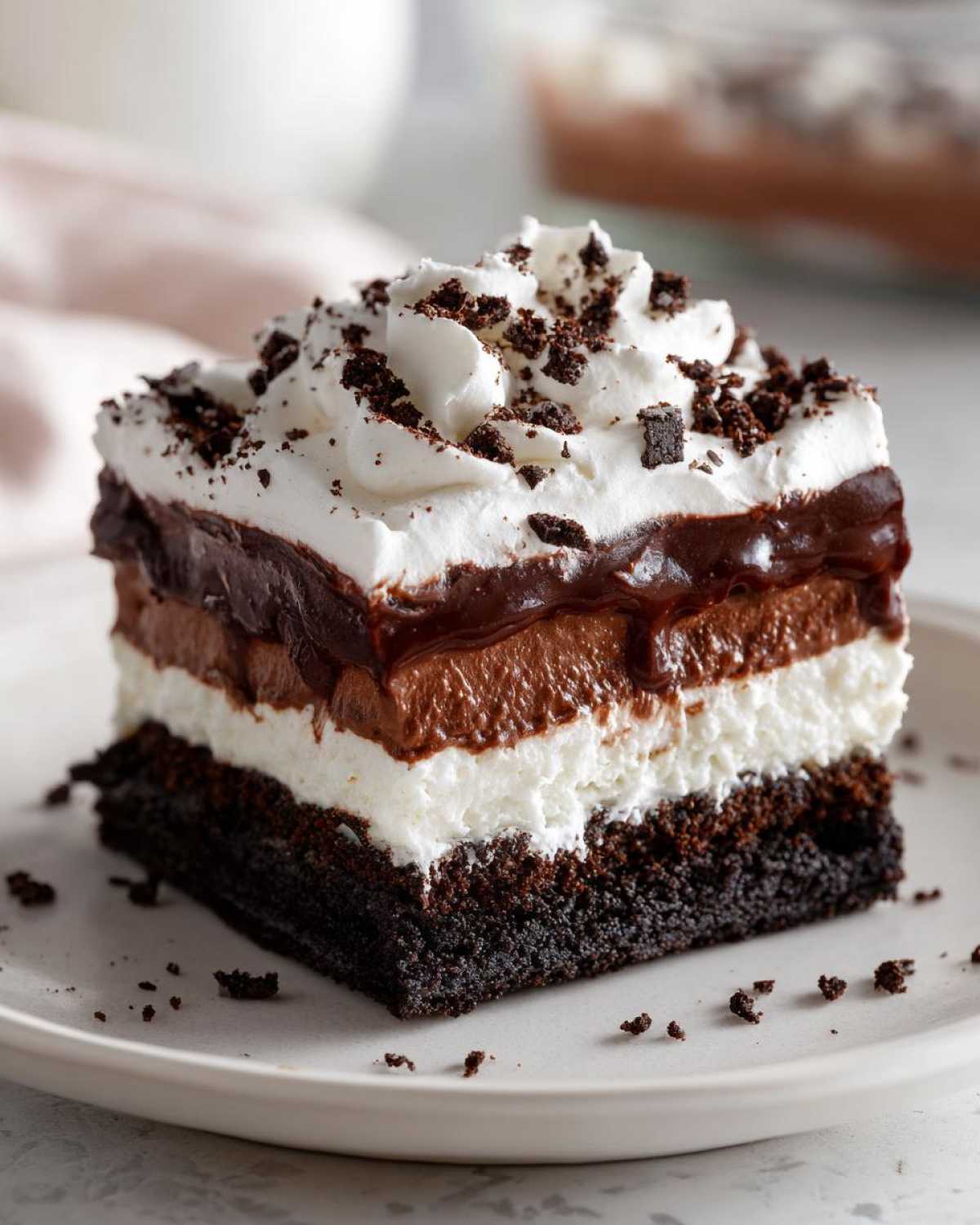 A square slice of rich chocolate lasagna featuring a dark crust, white layer, chocolate mousse, and whipped cream topping.