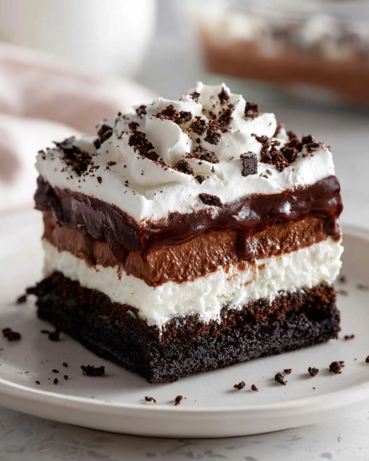 A square slice of rich chocolate lasagna featuring a dark crust, white layer, chocolate mousse, and whipped cream topping.