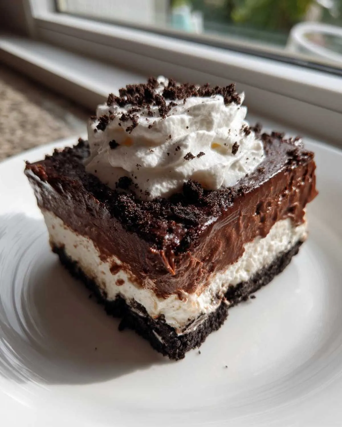 A square slice of rich chocolate lasagna with layers of crust, cream, and chocolate pudding, topped with whipped cream.
