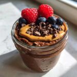 Close-up of chocolate overnight oats topped with peanut butter, fresh raspberries, blueberries, and chocolate shavings.