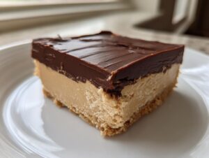 A square slice of rich chocolate peanut butter fudge with a thick chocolate topping on a white plate.