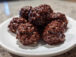 Close-up of several shiny, textured chocolate rice krispie balls piled on a small white plate.