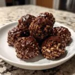 A close-up of several rich chocolate rice krispie balls drizzled with melted chocolate, served on a white dish.