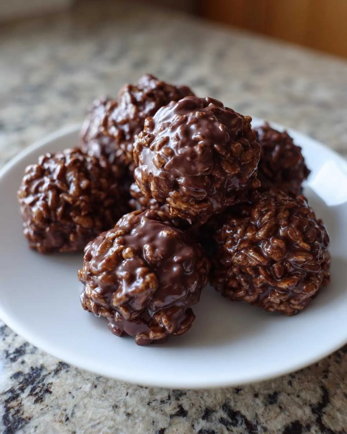 A pile of glossy, rich chocolate rice krispie balls resting on a small white plate.