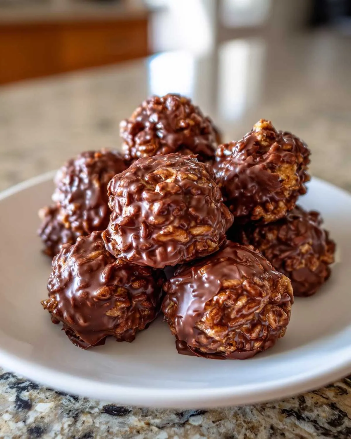 A close-up stack of glossy, chocolate-coated chocolate rice krispie balls resting on a white plate.