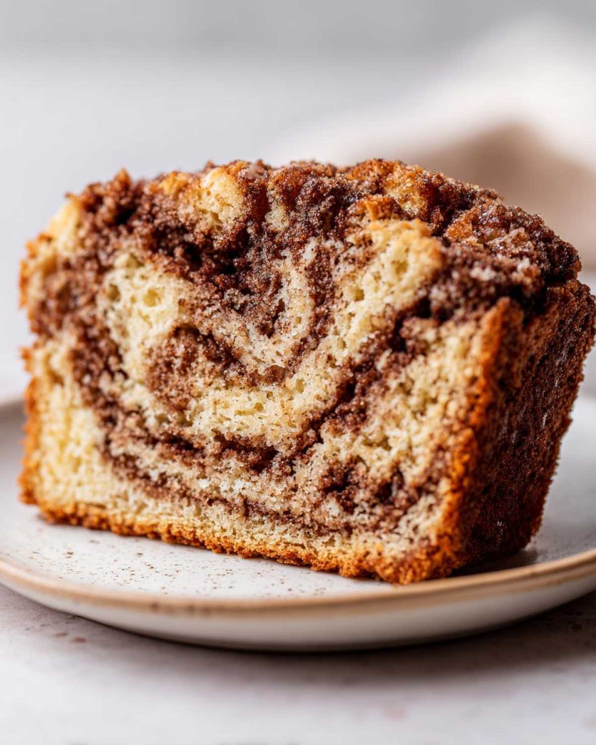 Close-up of a moist slice of cinnamon bread showing rich brown cinnamon swirls and a sugary topping.
