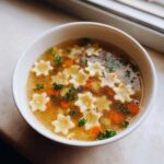 Close-up of a comforting bowl of pastina soup featuring star-shaped pasta, sliced carrots, and fresh parsley.