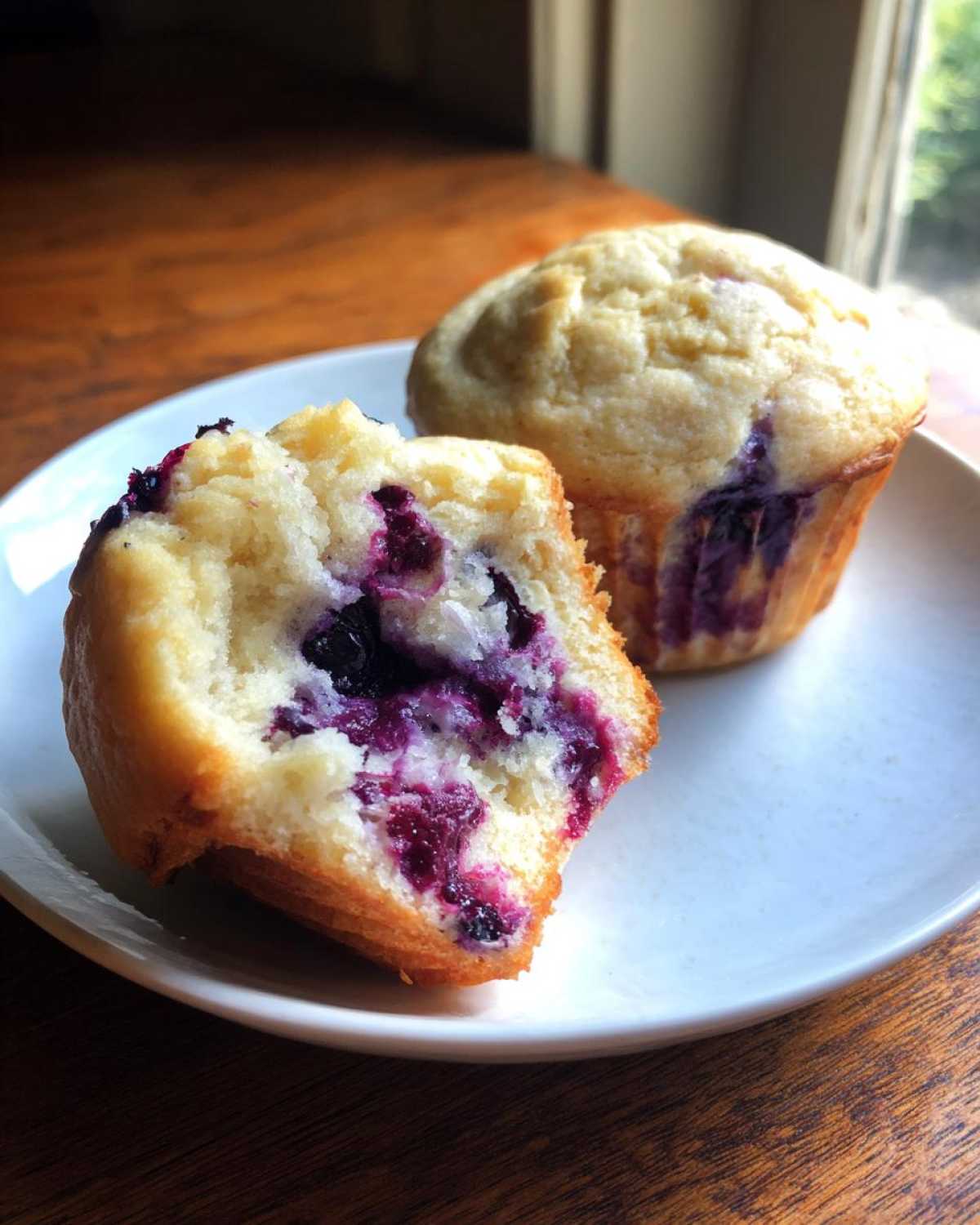 Close-up of two cottage cheese blueberry muffins, one cut in half showing the moist interior and burst blueberries.