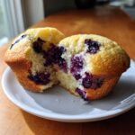 A close-up of a cottage cheese blueberry muffin broken in half, showing the moist, bright interior packed with blueberries.