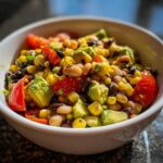 Close-up of fresh cowboy caviar recipe featuring black beans, corn, avocado, and tomatoes in a white bowl.