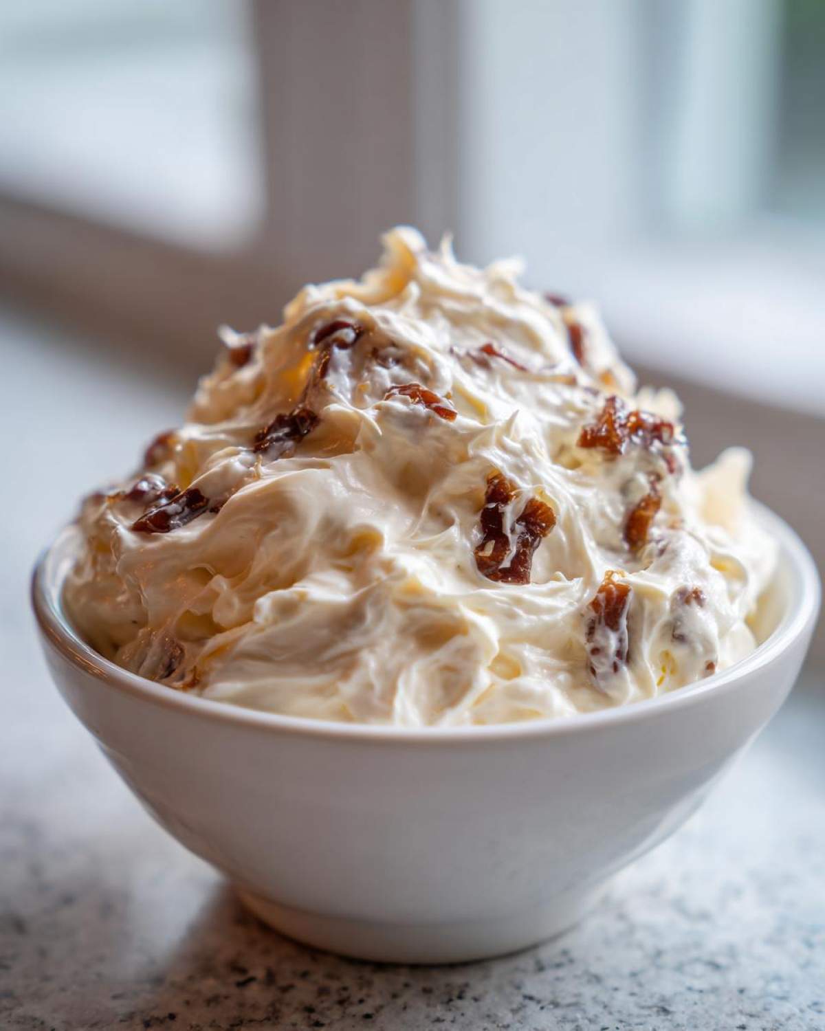 Close-up of a fluffy white bowl filled with creamy caramelized onion dip, featuring visible pieces of dark caramelized onion.