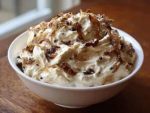 A close-up of creamy caramelized onion dip served in a white bowl, generously topped with rich, dark caramelized onions.