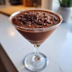 A creamy chocolate martini served in a coupe glass, generously topped with dark chocolate shavings.