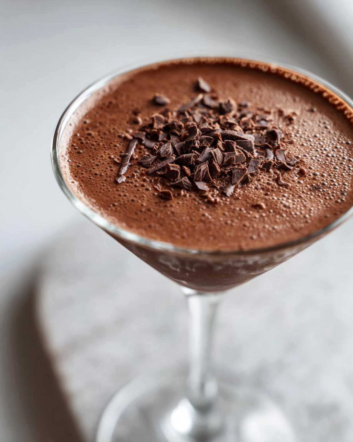 Close-up of a creamy chocolate martini in a glass, garnished with dark chocolate shavings.