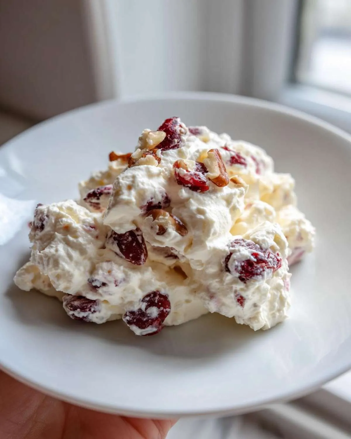 A scoop of fluffy, white cranberry salad mixed with dried cranberries and chopped pecans on a white plate.