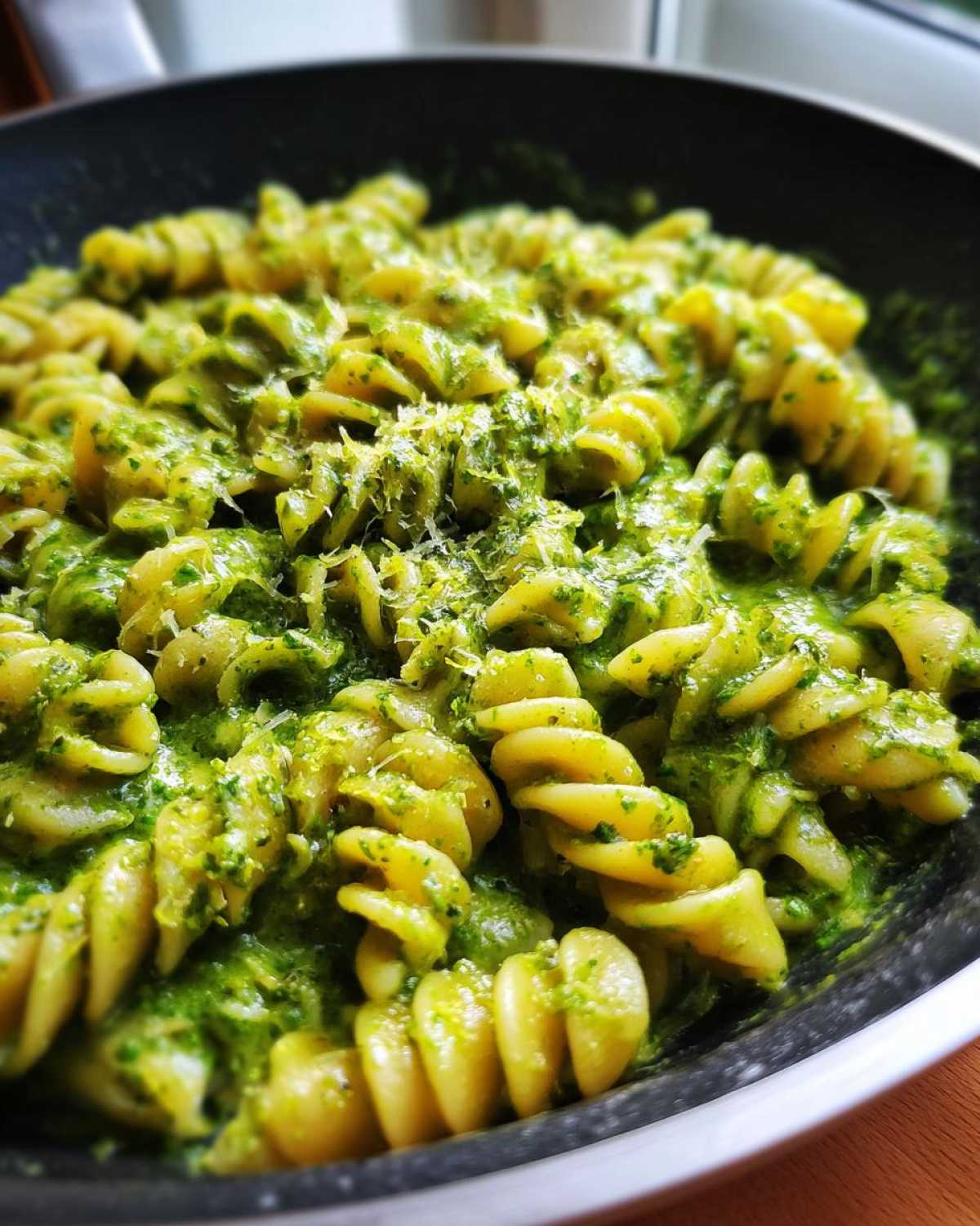Close-up view of fusilli pasta coated in vibrant green creamy pesto pasta sauce, topped with grated cheese.