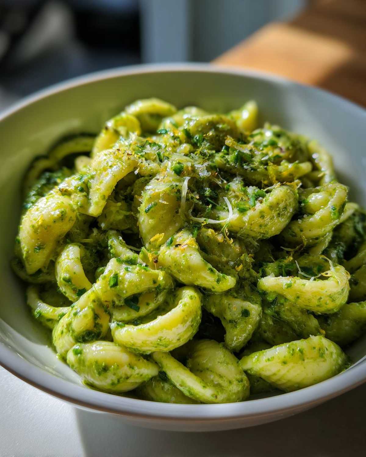 Close-up of orecchiette pasta coated in vibrant, creamy pesto pasta sauce, topped with cheese.