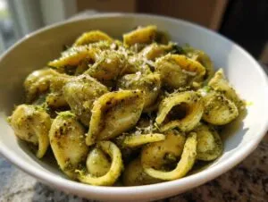 Close-up of a white bowl filled with creamy pesto pasta made with orecchiette or shell-shaped noodles.