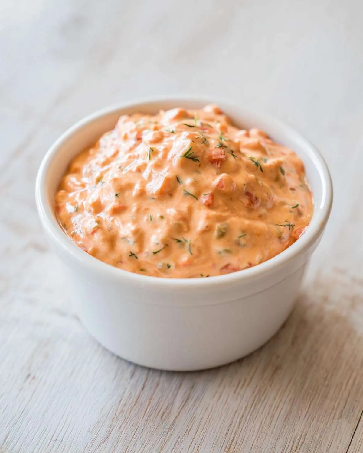 Close-up of creamy, orange-hued smash burger sauce with visible relish and dill flecks in a small white ramekin.