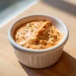 Close-up of creamy, orange-hued smash burger sauce speckled with herbs in a small white bowl.