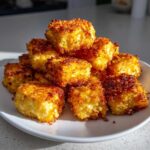A pile of golden brown, crispy air fryer tofu cubes stacked high on a white plate.
