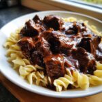 Close-up of tender crockpot beef tips smothered in rich brown gravy served over a bed of wide egg noodles.