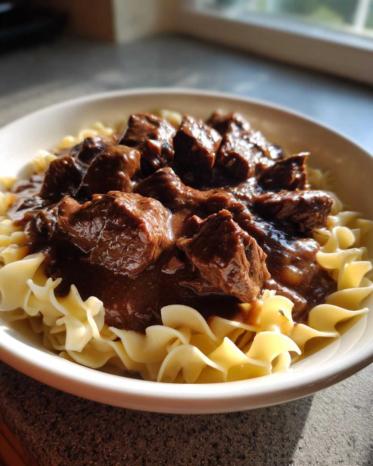 Close-up of tender crockpot beef tips smothered in rich brown gravy served over wide egg noodles.