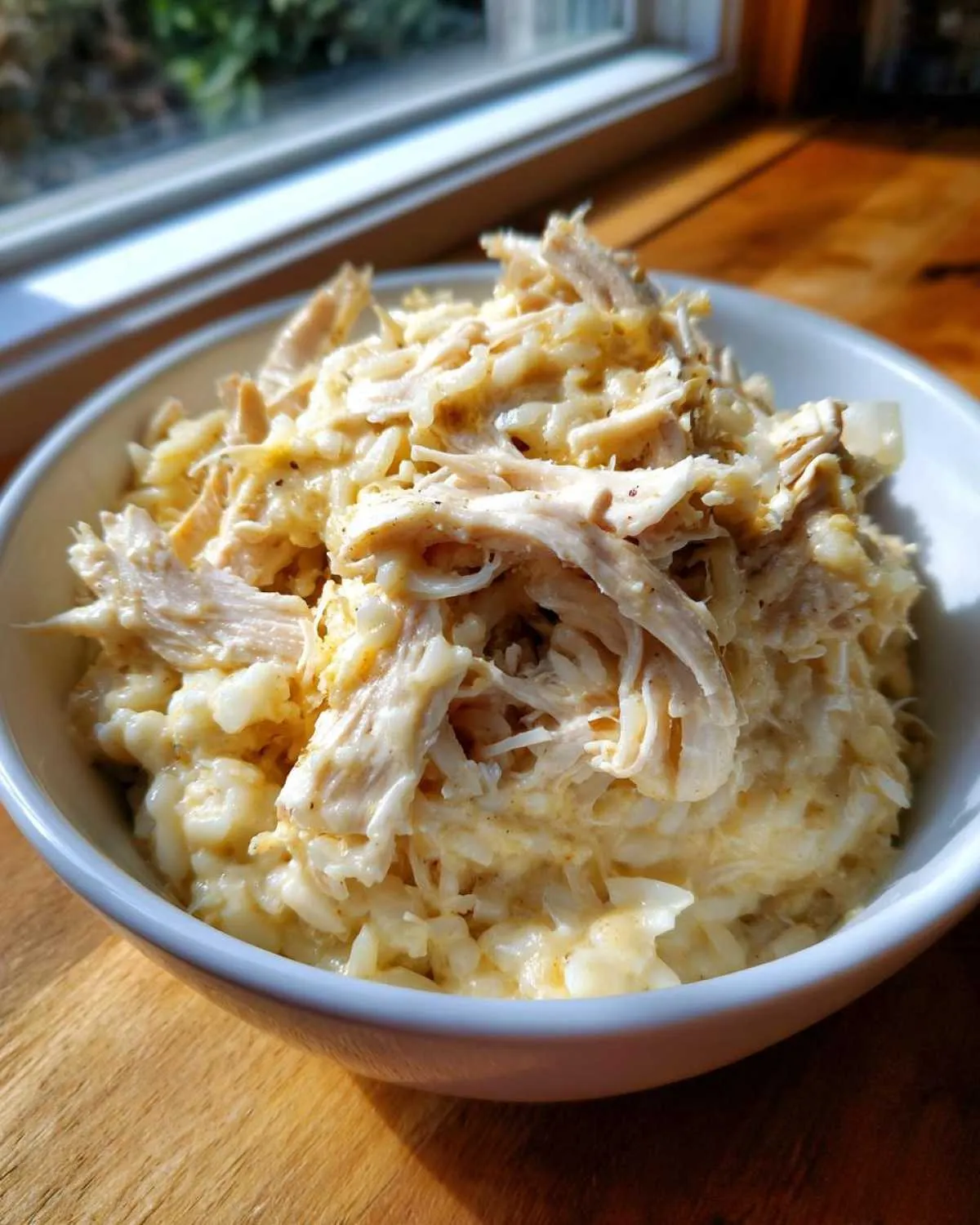 A white bowl filled with creamy crockpot chicken and rice, topped with shredded chicken.