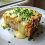 A thick slice of Eggs Benedict Casserole topped with rich hollandaise sauce and fresh chives.