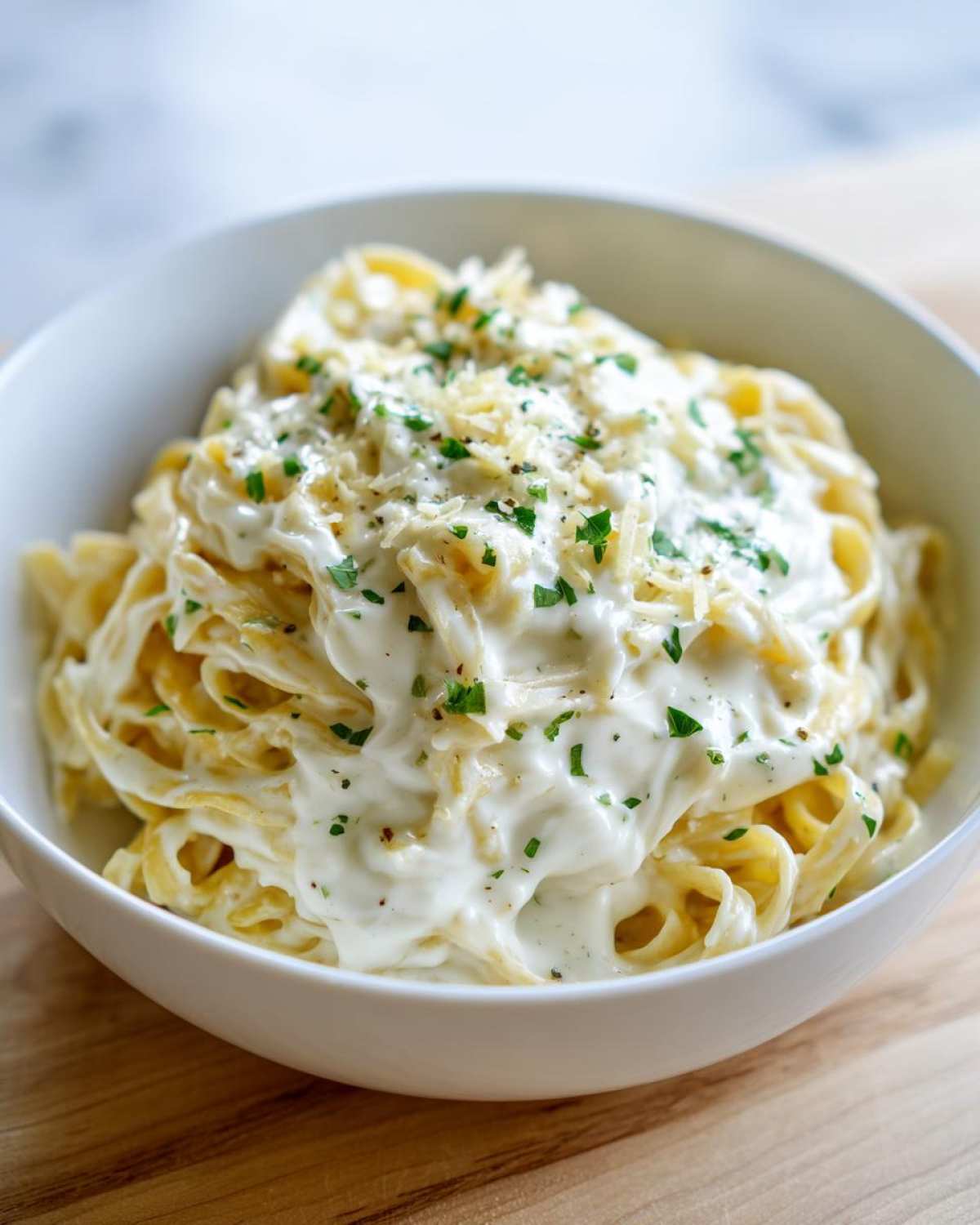 Close-up of fettuccine pasta generously coated in a rich, white cream sauce, topped with grated cheese and parsley.