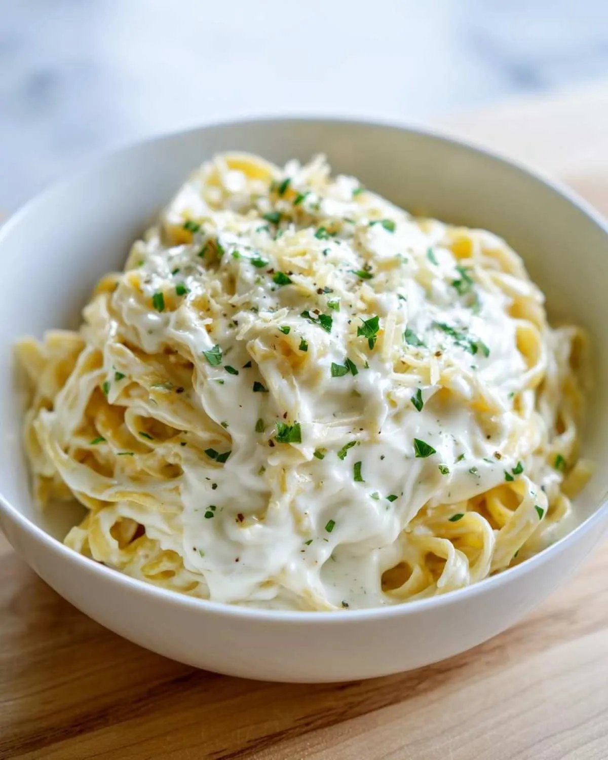 Close-up of fettuccine pasta generously coated in a rich, white cream sauce, topped with grated cheese and parsley.