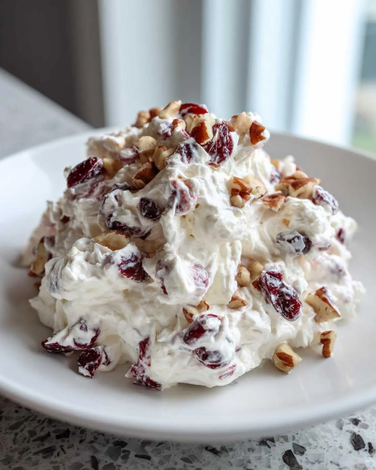 A mound of creamy, white cranberry salad mixed with dried cranberries and topped with chopped pecans.