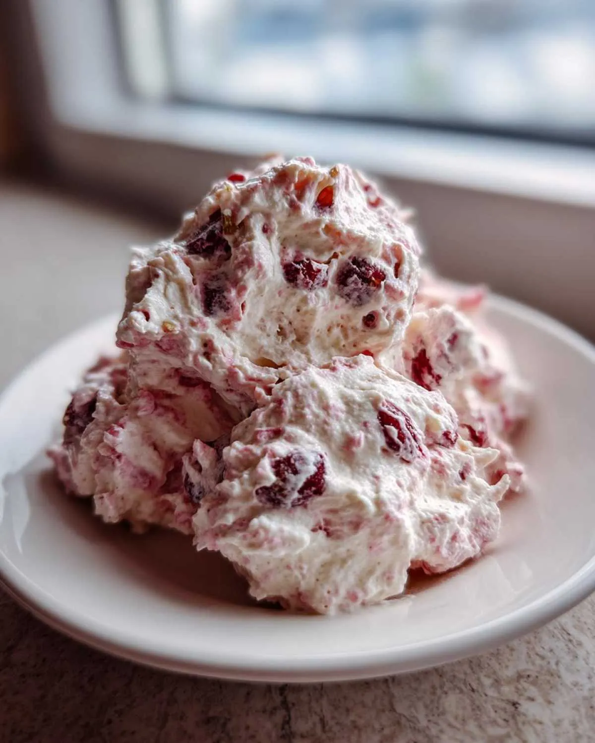 Three scoops of creamy, white cranberry salad mixed with visible red cranberries served on a small white dish.