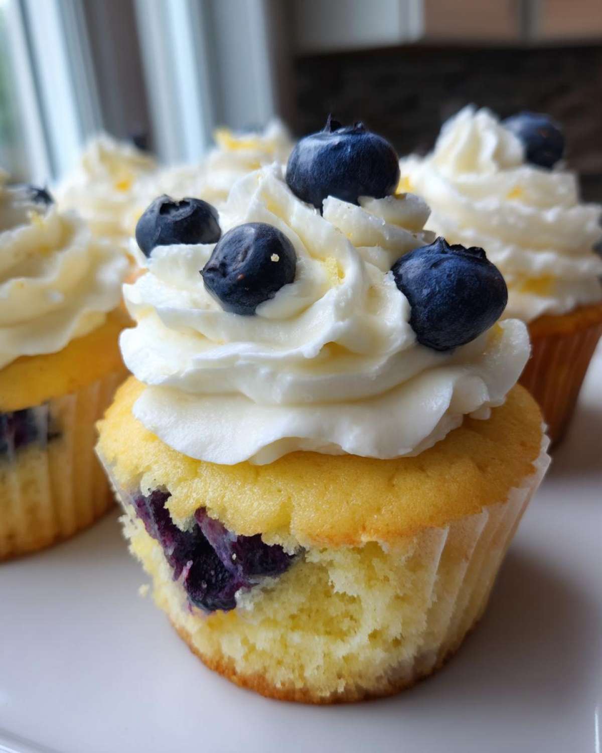Close-up of a fluffy lemon blueberry cupcake topped with white frosting and fresh blueberries.