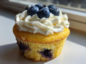 Close-up of a fluffy lemon blueberry cupcake topped with white frosting and fresh blueberries.