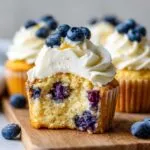 Close-up of a fluffy lemon blueberry cupcakes cut in half showing moist cake and blueberries, topped with cream cheese frosting.