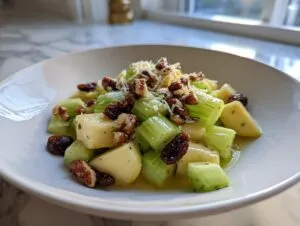 Close-up of a vibrant celery salad featuring chopped celery, apple chunks, pecans, and raisins in a light dressing.
