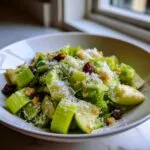 Close-up of a bowl containing fresh celery salad, topped with grated cheese, raisins, and croutons.