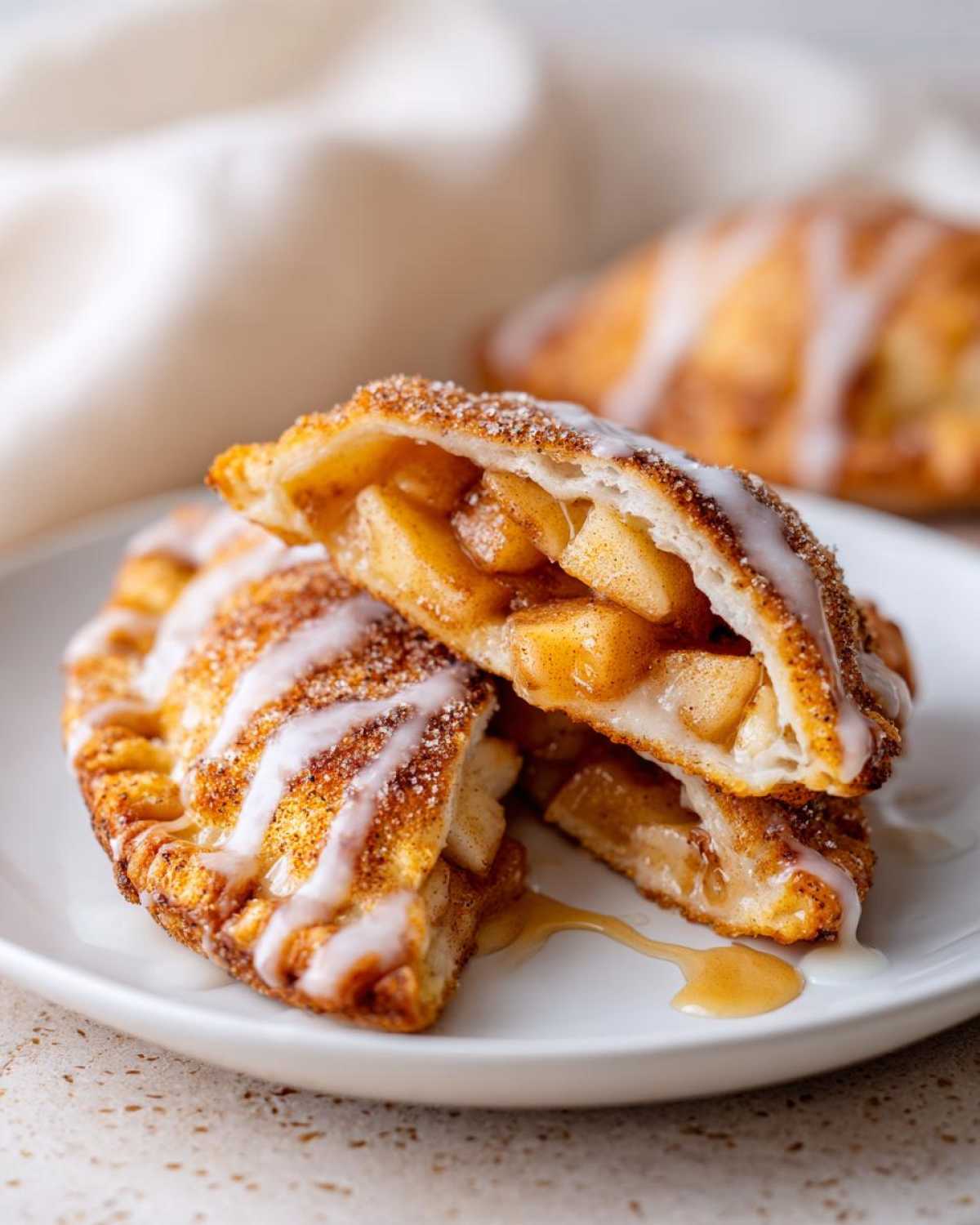 Close-up of two halves of fried apple pies stacked, showing cinnamon apples inside and drizzled with white glaze.