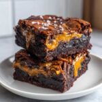 Two stacked, fudgy caramel brownies oozing with gooey caramel and topped with sea salt.