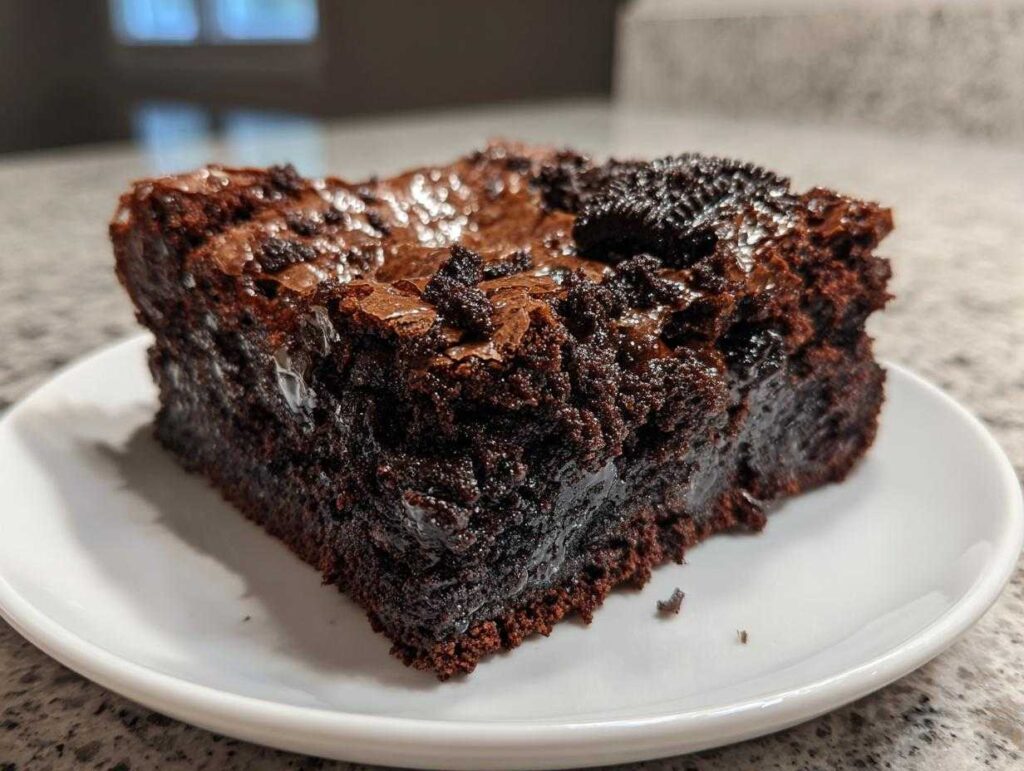 A close-up of a rich, fudgy square of oreo brownies topped with crushed cookie pieces.
