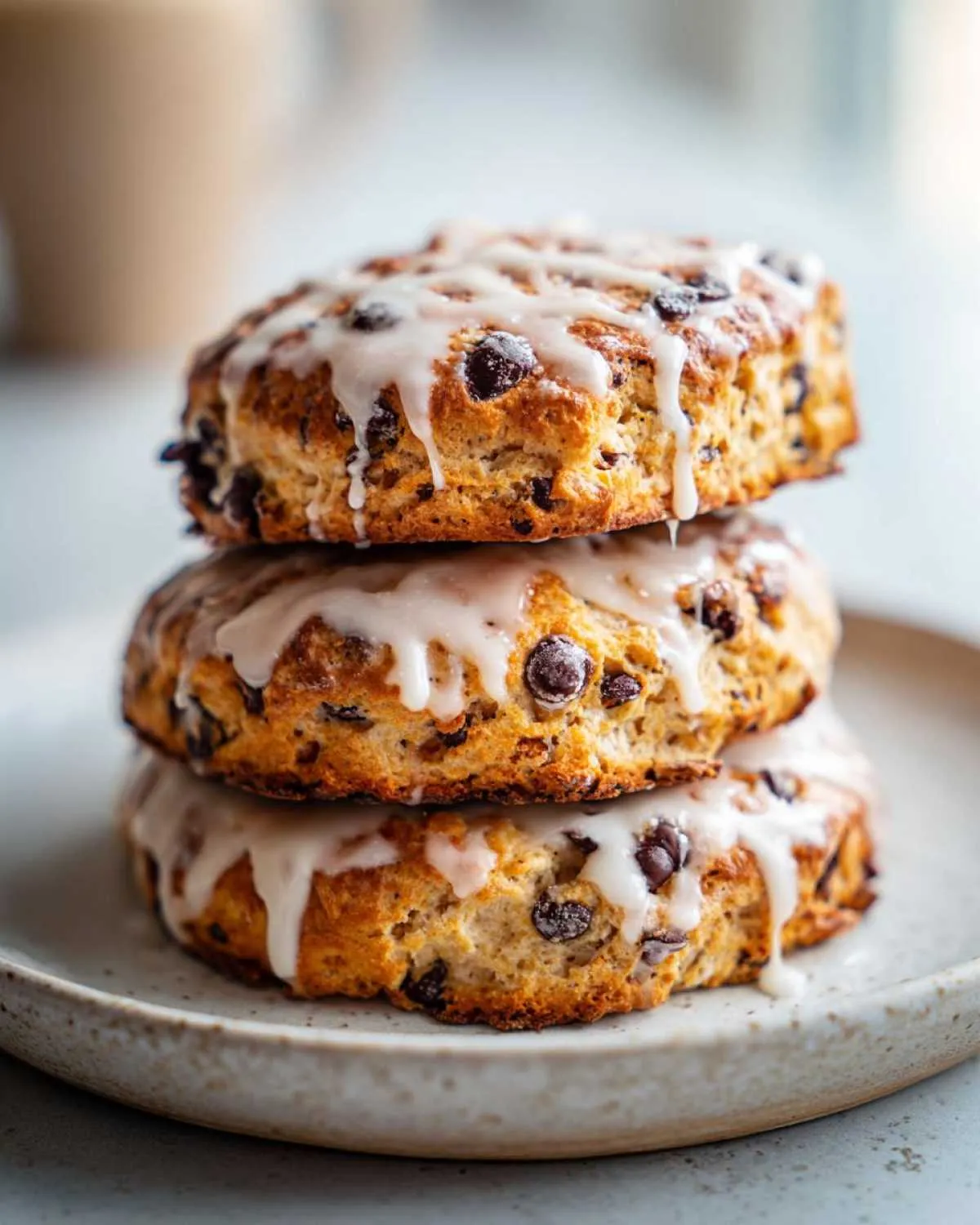 Three delicious chocolate chip scones stacked and drizzled with a white vanilla glaze.