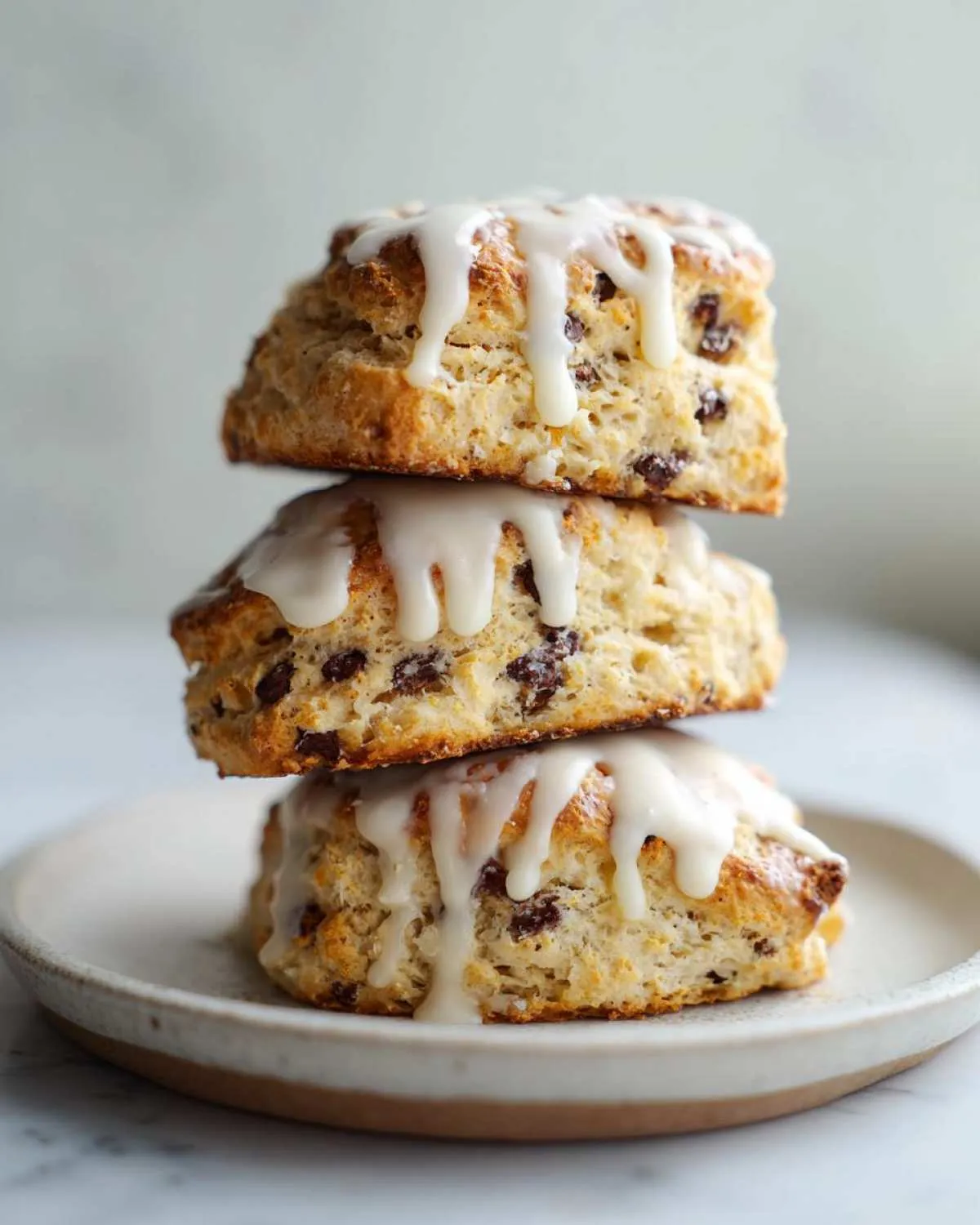 Three freshly baked chocolate chip scones stacked vertically and drizzled with white vanilla glaze.