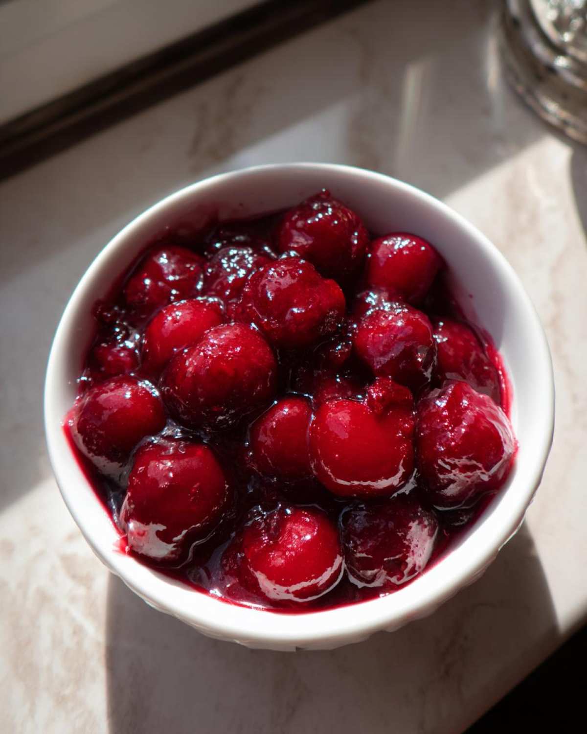 Close-up of glossy, vibrant red cherry pie filling with whole cherries in a white bowl.