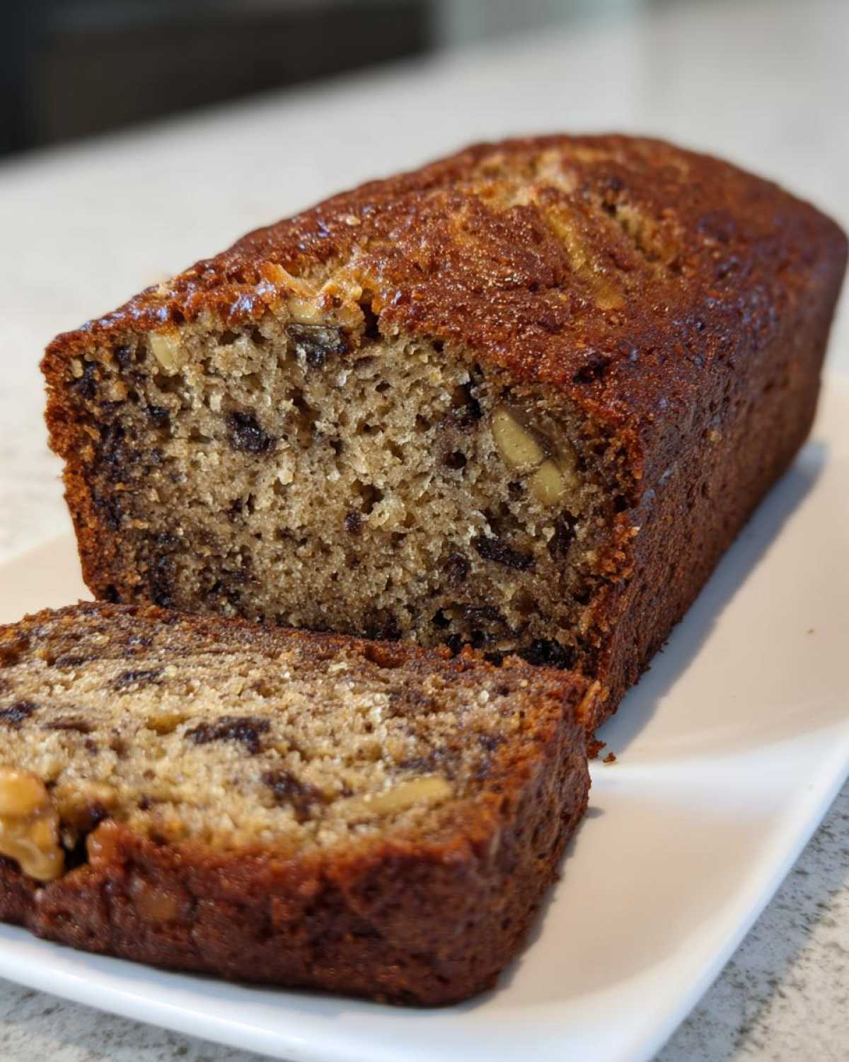 A close-up of a freshly baked greek yogurt banana bread loaf with one slice cut and resting against it.