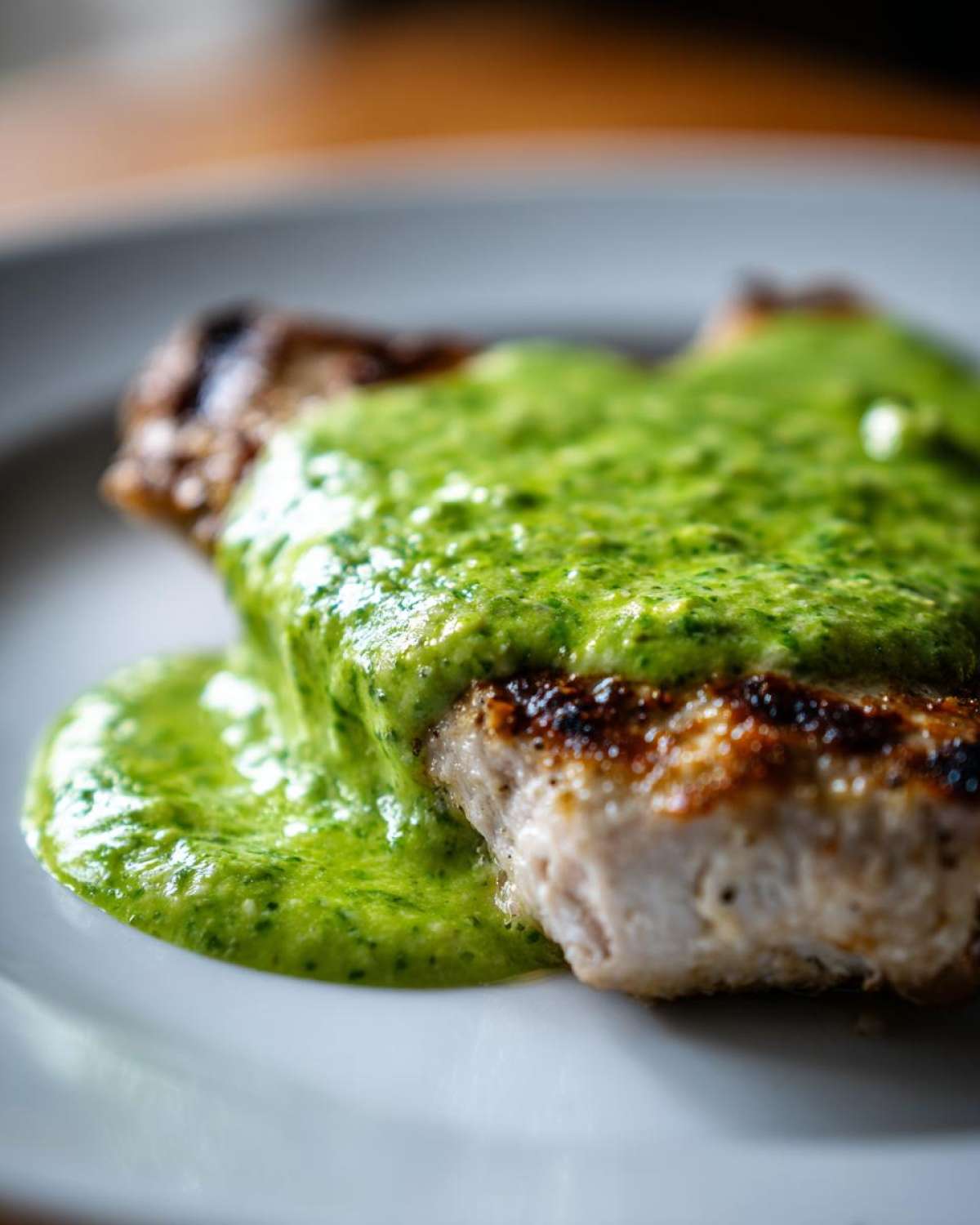 Close-up of a grilled piece of meat generously covered in a vibrant, green cilantro lime sauce on a white plate.